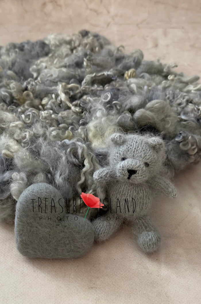 Close-up of a handcrafted knitted teddy bear and felted heart resting on a luxury curly wool newborn photography blanket.