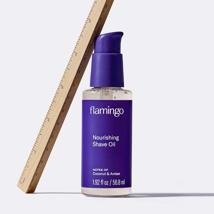 Mini shave oil with a ruler leaned against it on a white background.