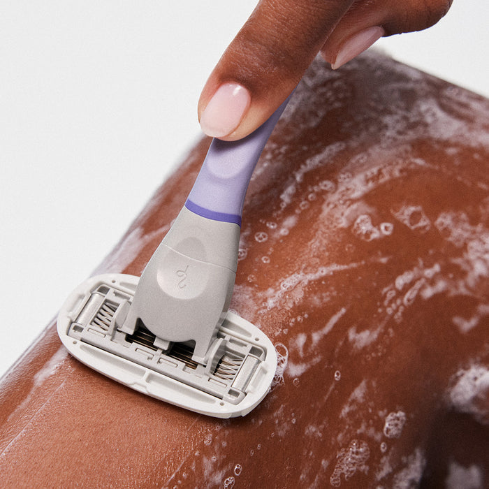 Person using the Lilac Original Razor and the Nourishing Shave Oil to shave their knee.