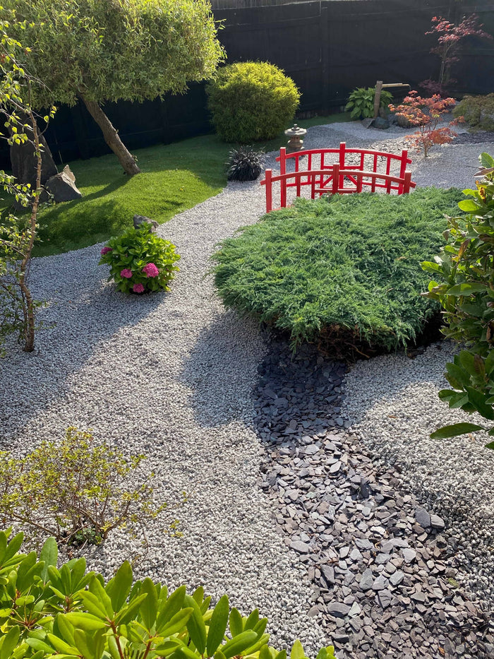 a zen garden with a red bridge, silver gravel ground cover and a path of blue slate cutting through