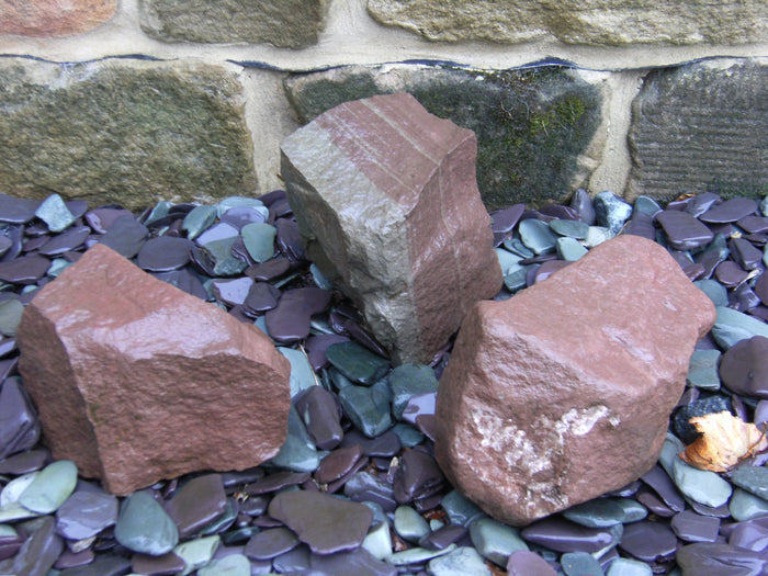 Three boulders placed on top of plum slate chippings, wet to reveal the true colours of the stone
